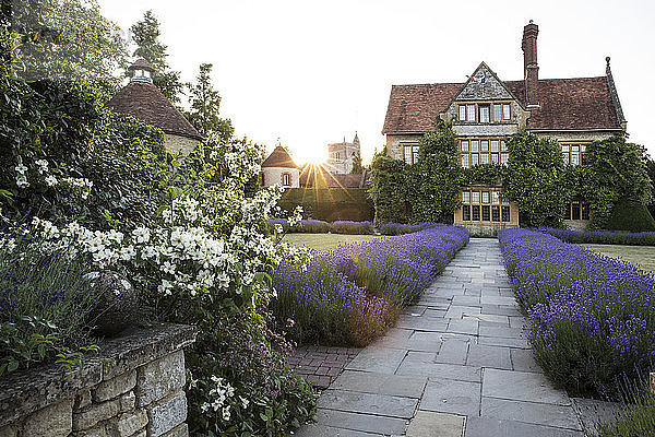 Blick auf das historische Herrenhaus aus einem ummauerten Garten mit Rasen  Weg und Blumenbeeten.
