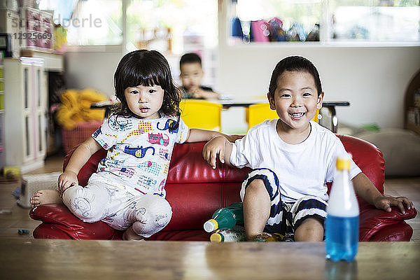 Lächelnder Junge und lächelndes Mädchen sitzen auf einem roten Sofa in einer japanischen Vorschule.