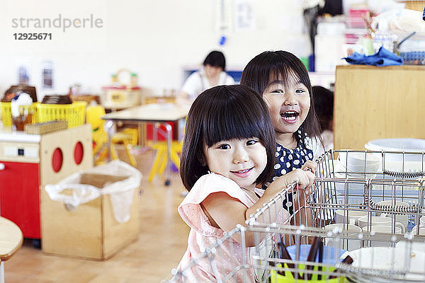 Zwei lächelnde Mädchen in einer japanischen Vorschule  die in die Kamera schauen.