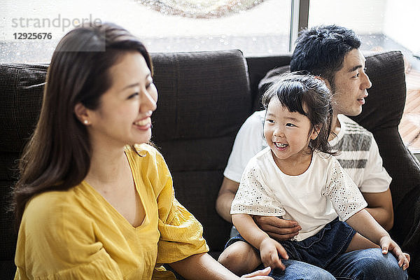 Porträt eines lächelnden japanischen Mannes  einer Frau und eines jungen Mädchens  die auf einem Sofa sitzen.