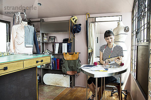 Japanische Modedesignerin  die am Schreibtisch sitzt und in ihrem Atelier arbeitet.