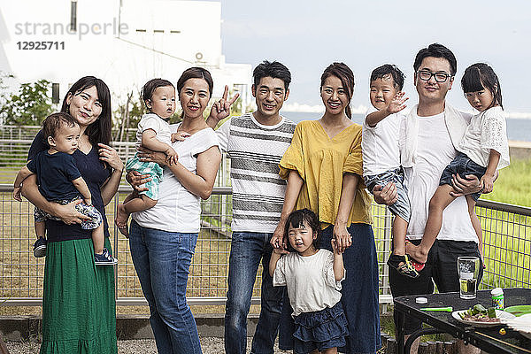Gruppenporträt japanischer Familien mit kleinen Kindern  die in einem Hintergarten stehen und in die Kamera lächeln.