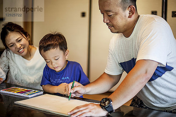 Japanische Frau  Mann und kleiner Junge sitzen an einem Tisch und zeichnen mit Farbstiften.
