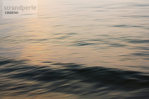 Detail der Wellen  die sich auf dem Wasser bilden  und eines Wasserrückens  der sich bei Sonnenuntergang dem Strand nähert.