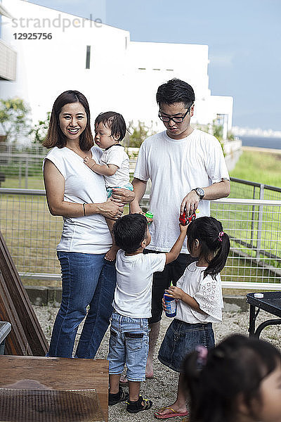 Porträt einer lächelnden japanischen Familie mit drei kleinen Kindern  die in einem Garten hinter dem Haus stehen.