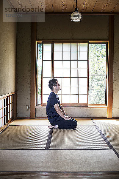 Japanischer Mann kniend auf Tatami-Matte in traditionellem japanischen Haus.