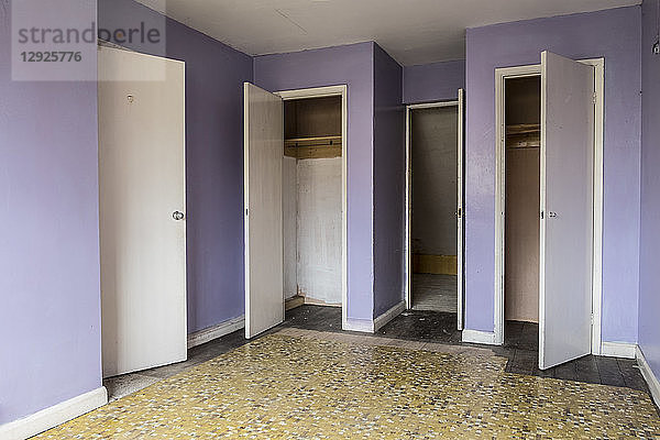 Innenansicht eines leeren Schlafzimmers mit gelbem Boden und fliederfarbenen Wänden in einem verlassenen Haus  weiße Schranktüren.