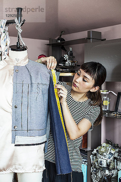 Japanische Modedesignerin  die in einem Atelier an einem Kleidungsstück nach dem Modell einer Schneiderin arbeitet.