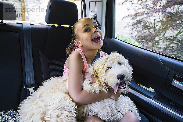 Mädchen mit Labradoodle-Welpe im Auto macht albernes Gesicht