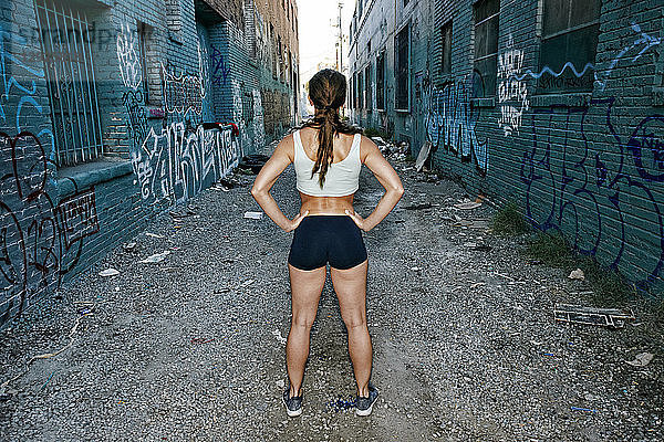 Rückansicht einer Athletin  die auf einer Straße steht  die von mit Graffiti bedeckten Gebäuden gesäumt ist.