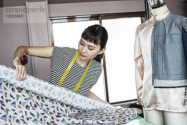 Japanische Modedesignerin  die in ihrem Atelier arbeitet und eine Stoffrolle hält.