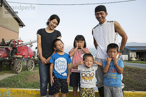 Porträt eines lächelnden japanischen Bauern  seine Frau und vier Kinder stehen in ihrem Hof  die Kinder ziehen vor der Kamera Gesichter.