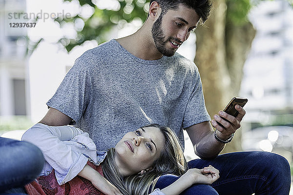 Mann benutzt ein Smartphone  während sich eine Frau auf seinem Schoß entspannt