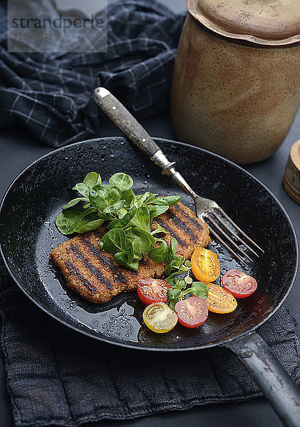 Gegrilltes veganes Bohnenhack-Steak mit Tomaten und Salat in einer Pfanne