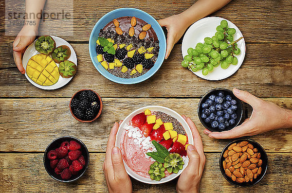 Männer- und Kinderhände mit gesunden Frühstücks-Smoothie-Bowls mit Früchten und Beeren