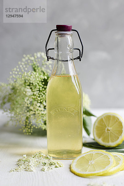 Holunderblüten-Sirup in einer Vintage-Flasche  mit frischen Holunderblüten und Zitrone im Hintergrund