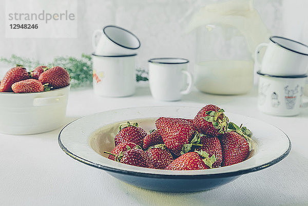 Ein Teller mit frischen Erdbeeren  Tassen  Milch in einem Glasgefäß auf einem weißen Hintergrund