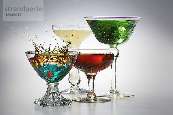 Vier verschiedene Cocktails in Gläsern vor einem grauen Hintergrund