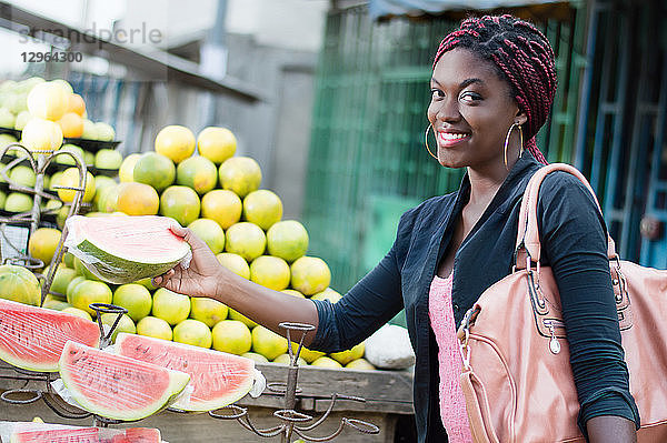 Eine lächelnde junge Frau greift auf einem Straßenmarkt nach einer Scheibe reifer Früchte.