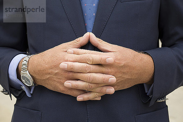 Nahaufnahme der Hände eines Mannes im Anzug mit voreinander verschränkten Fingern.