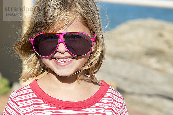 Porträt eines hübschen kleinen lächelnden blonden Mädchens mit Brille von rosa Erwachsenen.