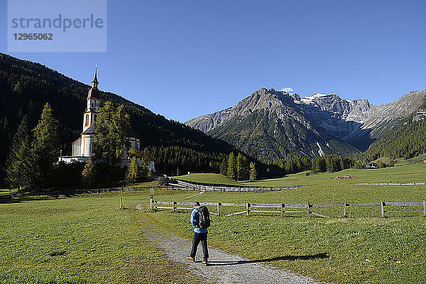 Österreich  Tirol  Obernberg ein Mann geht auf die Barockkirche St. Nikolaus zu  die am Fuße des Gschnitzer Tribulaun steht