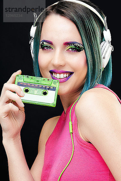 Porträt einer lächelnden jungen Frau  die eine Audiokassette in der Hand hält