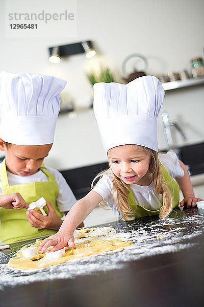 Zwei junge Kinder glücklich Kinder Junge und Mädchen Familie mit Schürze und Kochmütze Vorbereitung lustige Cookies in der Küche zu Hause.