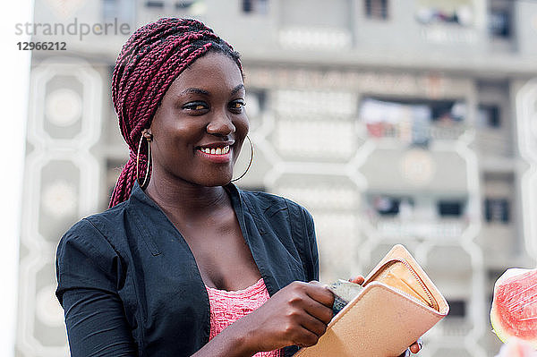 eine lächelnde junge Frau  die Geld aus ihrem Portemonnaie nimmt.