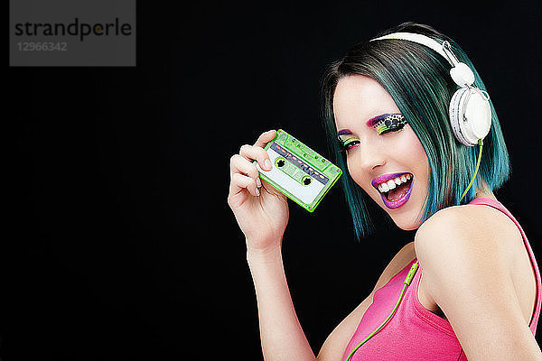 Porträt einer lächelnden jungen Frau  die eine Audiokassette in der Hand hält