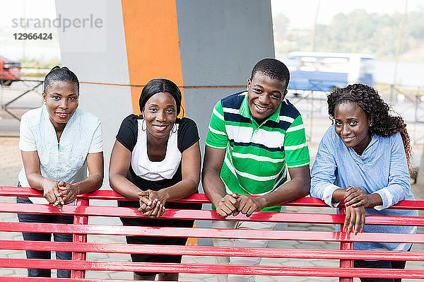 Diese Gruppe junger Freunde in einem Park  die sich mit einem schönen Lächeln an eine Bank lehnen.