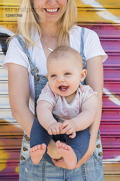 Lächelndes kleines Mädchen  das von seiner Mutter gehalten wird