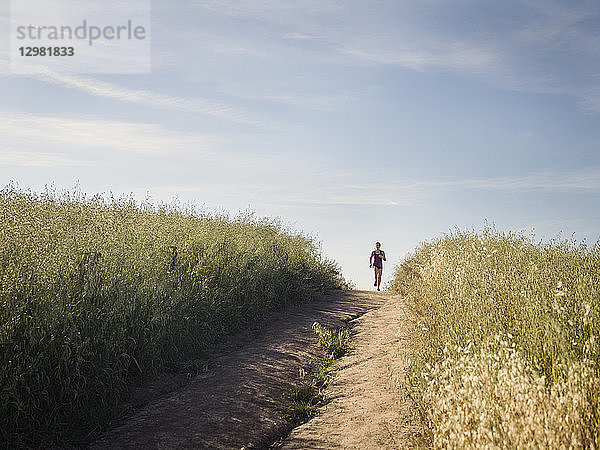 Frau joggt auf einem Weg durch ein Feld