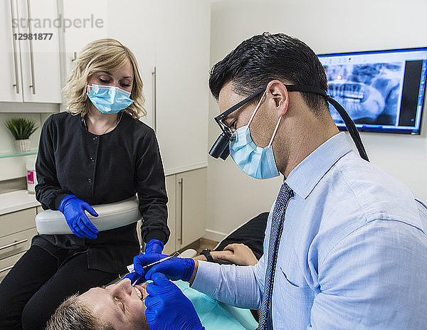 Zahnarzt und Zahnarzthelferin bei der Untersuchung der Zähne eines Patienten