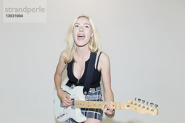 Überschwängliche junge Frau spielt E-Gitarre