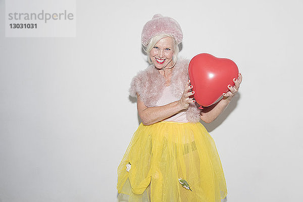 Porträt einer lächelnden  selbstbewussten älteren Frau  die einen Ballon in Herzform hält
