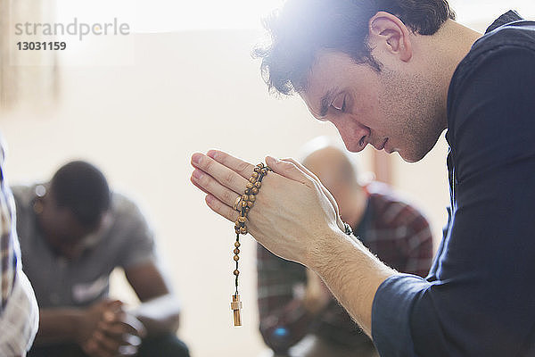 Gelassener Mann betet mit Rosenkranz in Gebetsgruppe