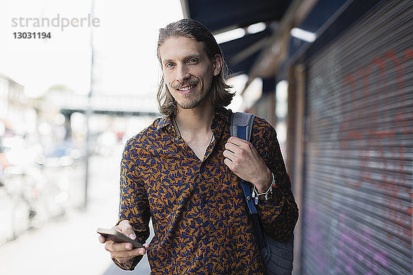 Porträt selbstbewusster Hipster-Mann mit Smartphone auf städtischem Bürgersteig