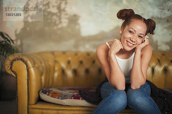 Porträt einer lächelnden  selbstbewussten jungen Frau  die auf einem Sofa sitzt