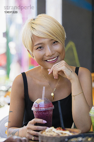 Porträt einer lächelnden  selbstbewussten jungen Frau  die in einem Straßencafé einen Smoothie trinkt