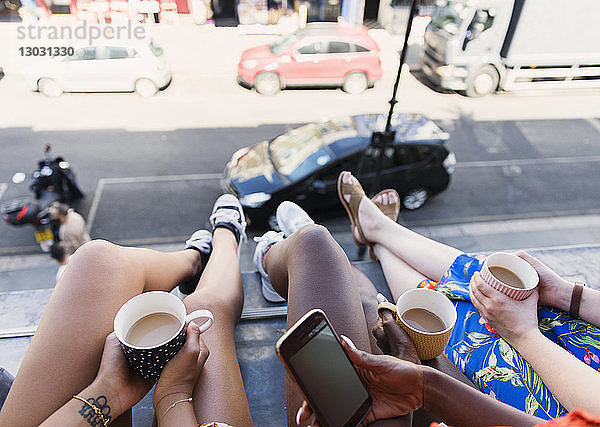 Freundinnen  die Kaffee trinken und die Beine aus dem Fenster einer städtischen Wohnung baumeln lassen