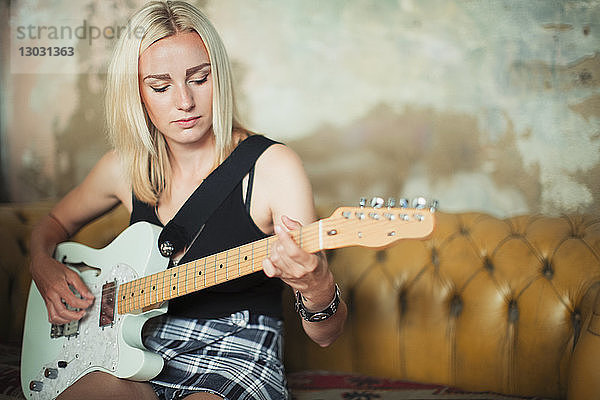 Junge Frau spielt E-Gitarre auf dem Sofa