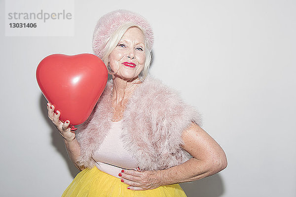 Porträt selbstbewusste ältere Frau im Pelz  die einen Ballon in Herzform hält