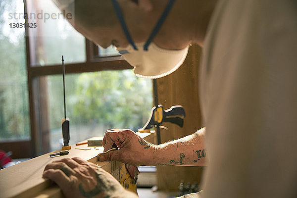 Nahaufnahme eines Bauarbeiters mit Tattoos  der eine Holzplatte untersucht