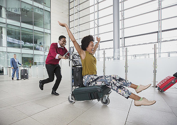 Verspieltes Paar läuft mit Gepäckwagen im Flughafen