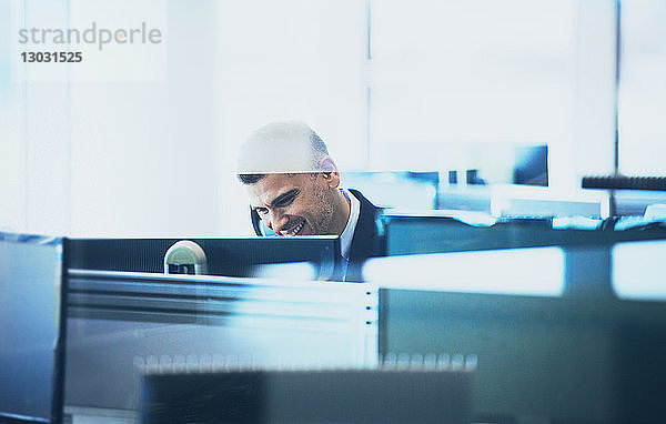 Lächelnder Geschäftsmann  der am Computer im Büro telefoniert