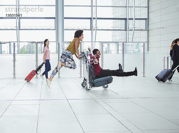 Verspieltes Paar schiebt Gepäckwagen im Flughafen