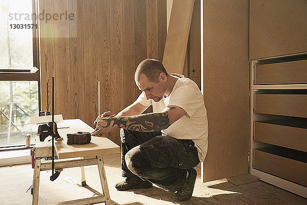 Bauarbeiter mit Tätowierung  der eine Holzplatte in einem Haus misst