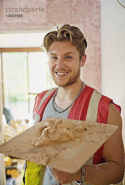 Porträt lächelnder  selbstbewusster junger Bauarbeiter beim Verputzen