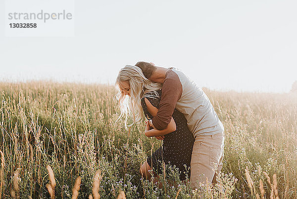 Romantischer Mann umarmt seine Freundin im sonnenbeschienenen langen Grasfeld